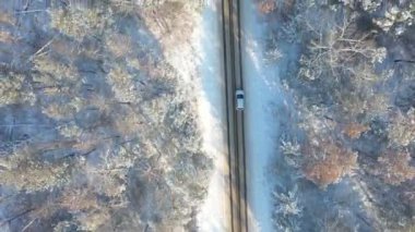 Kış günü ormanın güzel kırsal kesiminde SUV sürüyordu. Karla kaplı buzlu yolda uçan beyaz arabanın görüntüsü. Otomotiv üzerinde uçmak manzaralı bir yolda ilerlemek. Üst görünüm