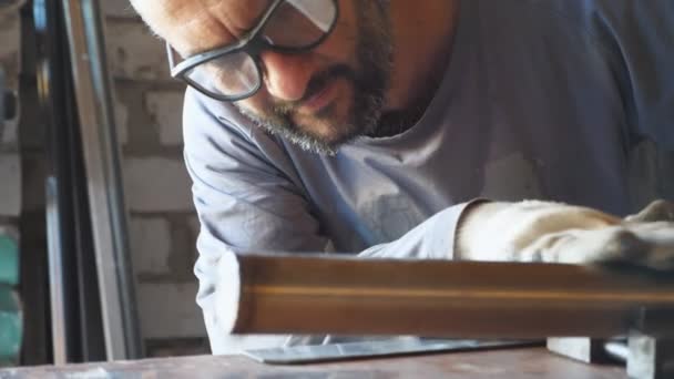 Reparador adulto em óculos de proteção examinando um tubo fixo na mesa na oficina. Mecânico masculino se preparando para soldar detalhes de metal na garagem. Conceito de serviço de manutenção. Fechar câmera lenta — Vídeo de Stock