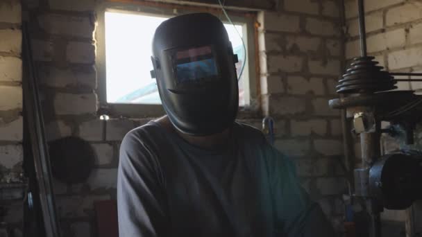 Portret dorosłego spawacza otwiera maskę ochronną po zakończeniu pracy i spojrzeniu w kamerę w warsztacie. Profesjonalny mechanik z brodą pracujący w garażu. Zamknij Powolny ruch — Wideo stockowe