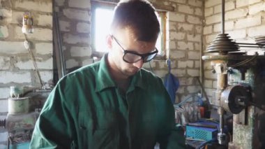 Üniformalı erkek tamirci atölyede metal işleriyle uğraşıyor. Garajda işini yapan koruyucu gözlüklü genç bir tamirci. Bakım hizmeti kavramı. Yavaşça kapat.