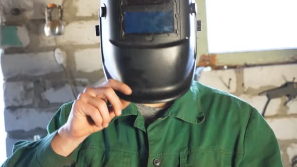 Detailní záběr samčího svářeče otvírá ochrannou masku a upevňuje některé kovové části v dílně. Mladý mechanik v pracovních oděvech pracující v garáži. Koncept údržby. Jeřáb vystřelil Zpomalený pohyb — Stock video