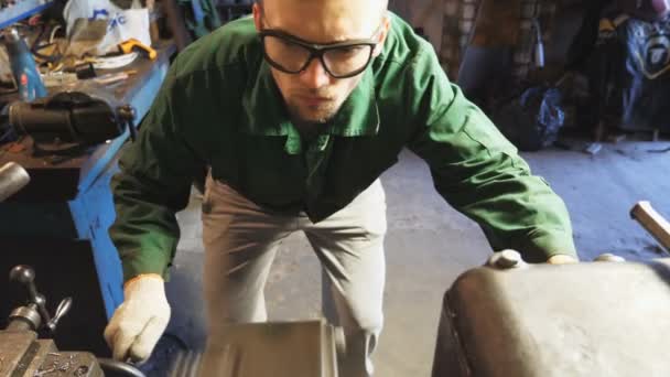 保護アイウェアの男性メカニックは、ガレージで金属を処理するために旋削旋盤を使用しています。彼のワークショップで古いワークベンチで制服を着た修理工。職場でのフライス盤の仕事。スローモーション — ストック動画