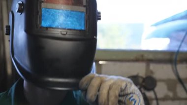 Mutlu kaynakçı işini bitirdikten sonra koruyucu maskeyi açar. İş kıyafetlerinde gülümseyen ve kameraya bakan tamirci portresi. Atölyede çalışan sakallı bir tamirci. Dolly vurdu.