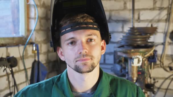 Retrato del joven reparador cansado con máscara protectora abierta en su cabeza mirando a la cámara en su garaje. Mecánico profesional en ropa de trabajo trabajando en taller. Concepto de servicio de mantenimiento. De cerca. — Vídeo de stock