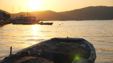 Dalgalarda sallanan balıkçı teknesinden körfezin güzel manzarası. Deniz yüzeyinde yüzen balıkçı gemileri ve arka planda günbatımı. Altın güneş ışığı okyanus ortamını aydınlatıyor. Manzaralı deniz manzarası