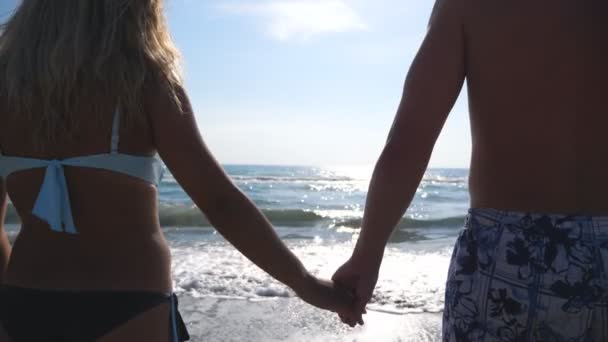 Männliche und weibliche Hände halten sich an einem wunderschönen Meeresgrund. Ein Liebespaar steht mit verschränkten Armen am Strand und genießt die herrliche Aussicht. Paar verbringt Zeit gemeinsam in den Sommerferien — Stockvideo