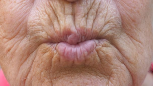 Close up lips of mature grandmother. Mouth of elder grandma sends air kiss into camera. Senior woman with wrinkled skin does kissing gesture. Slow motion — Stock Video
