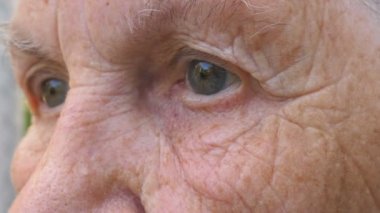 Yaşlı büyükannenin portresi hüzünlü bir manzarayla uzaktan görünüyor. Etrafında kırışıklıklar olan olgun kadınların gri gözlerini kapat. Yaşlı büyükannenin kederli yüz ifadesi