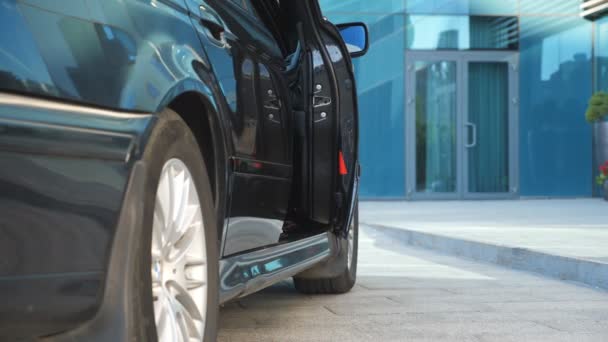 L'uomo d'affari apre la porta e scende dalla macchina vicino a un moderno edificio per uffici. Il giovane uomo d'affari scopre la porta dell'automobile. Il tizio in giacca e cravatta esce dalla Black Auto. Pendolari al lavoro. Rallentatore Close up — Video Stock