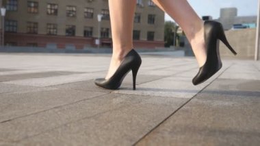 Güneşli bir günde şehir meydanında yürüyen yüksek topuklu siyah ayakkabılı zayıf kadın bacakları. Yüksek topuklu ayakkabılı genç iş kadınının ayakları şehir sokağına çıkıyor. Düşük açı görünümü Yavaş çekim kapat