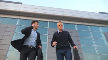 Açık havada başarılı bir iş anlaşması yaptıktan sonra elinde evrak çantasıyla dans eden iki genç iş adamının düşük açılı görüntüsü. Ofis yakınlarındaki başarılarını kutlayan neşeli meslektaşlar.