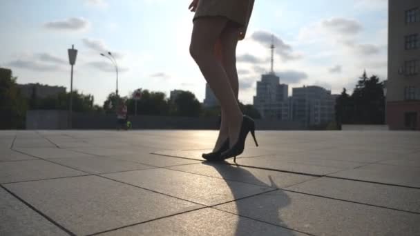 Pernas femininas finas em sapatos pretos em saltos altos andando na praça da cidade ao pôr do sol. Pés de mulher de negócios jovem em calçado em salto alto que vai na rua urbana. Visão de ângulo baixo Movimento lento Fechar — Vídeo de Stock
