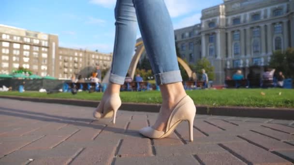 Weibliche Beine in Stöckelschuhen, die in städtischen Straßen spazieren gehen. Füße einer jungen Frau in hochhackigen Schuhen, die in der Stadt unterwegs ist. Mädchen tritt auf Gehweg. Niedrige Engel-Ansicht Zeitlupe Nahaufnahme