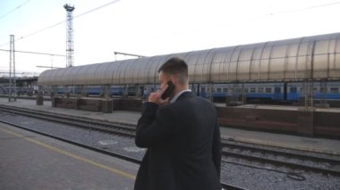 Başarılı bir iş adamı tren istasyonunda yürüyor ve telefonla konuşuyor. Demiryolu yakınlarında gezinen ve iş konuşması yapan yakışıklı bir adam. Adam dışarı çıkıp cep telefonuyla konuşuyor. Yavaş çekim