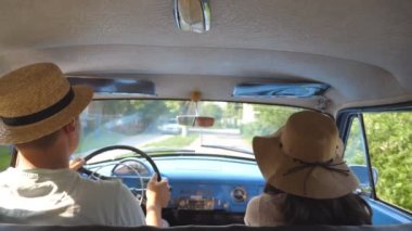 Klasik klasik bir arabayla köy yolunda araba kullanan şapkalı genç bir çift. Tanınmayan bir çift eski arabaya biniyor. Bir erkek ve kadın retro bir otomobilin ön koltuğunda oturuyorlar. Trip konsepti. Yavaş çekim