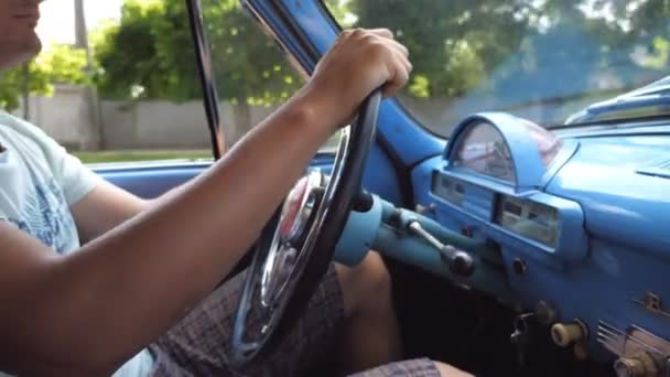 Nierozpoznany mężczyzna trzymający się za ręce na kierownicy i jeżdżący retro samochodem po wiejskiej drodze w słoneczny letni dzień. Młody człowiek w swoim starym niebieskim samochodzie. Zamknij Widok z boku Spowolnienie ruchu — Wideo stockowe