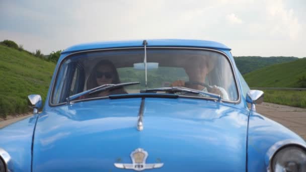 Jong stel in hoeden rijden in een vintage auto tijdens de zomer reizen. Man en vrouw zitten op de voorbank van een oude retro auto tijdens de rit. Concept van road trip op vakantie. Slow motion Close-up Vooraanzicht — Stockvideo