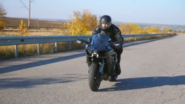 Jovem montando na moderna moto esportiva na rodovia de outono. Motociclista correndo sua motocicleta na estrada rural. Um tipo a conduzir bicicleta durante a viagem. Conceito de liberdade e aventura.Vista frontal Movimento lento — Vídeo de Stock