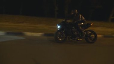 Akşam caddesinde modern siyah spor motosikletli bir adam hızlı gidiyor. Motosikletli, boş yolda motosikletiyle yarışıyor. Farları açık bisiklet süren adam. Özgürlük kavramı. Yan görünüm