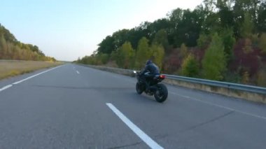 Sonbahar otobanında motosiklet süren motosikletliyi takip edin. Motosikletli, kır yolunda motosikletiyle yarışıyor. Yolculuk sırasında bisiklete binen adam. Özgürlük ve macera kavramı. Hava görüntüsü