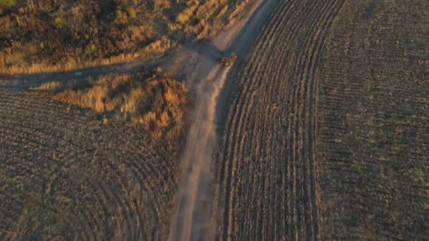 Letecký záběr farmářského džípu projíždějícího prázdnou venkovskou cestou mezi poli. Terénní vozidlo jede za soumraku po prašné cestě. Létání nad autem na venkově v letní den. Horní pohled — Stock video