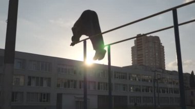 Erkek jimnastikçi silueti açık havada amuda kalkarak şınav çekiyor. Paralel barlarda dublörlük yapan genç bir atlet. Güçlü kaslı adam spor alanında performansını sergiliyor. Yavaş çekim