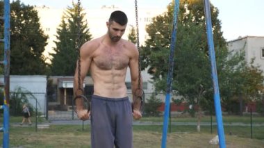 Spor sahasında jimnastik halkalarında haç yapan güçlü bir atlet. Kaslı üstsüz sporcu dışarıda sert gösteriler sergiliyor. Genç erkek jimnastikçi akrobatik egzersizler yapıyor. Sportif yaşam tarzı kavramı