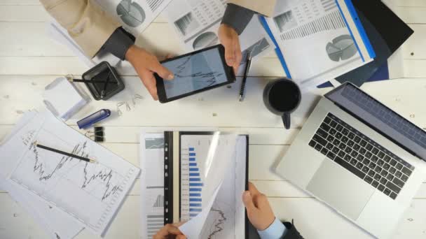 Κορυφαία προβολή ανδρικά χέρια δύο νέων επιχειρηματιών ελέγχοντας γραφήματα και συζητώντας οικονομικές εκθέσεις στο γραφείο. Επιτυχημένοι συνάδελφοι που κάθονται στο τραπέζι και αναπτύσσουν ένα νέο επιχειρηματικό σχέδιο — Αρχείο Βίντεο