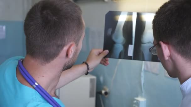 Le médecin se consulte. Deux médecins masculins regardent la photo IRM et en discutent. Travailleurs médicaux à l'hôpital à la recherche et l'analisation des empreintes radiographiques. Fermer Vue arrière arrière — Video