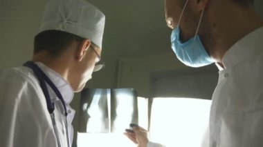 Kafkasyalı iki doktor MRI resmine bakıp bunu tartışıyor. Erkek doktorlar röntgen görüntülerine bakarken birbirlerine danışıyorlar. Hastanedeki tıp çalışanları röntgen izlerini inceliyor. Arka plan görünümü