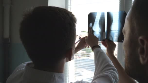 Le médecin se consulte. Travailleurs médicaux à l'hôpital à la recherche et l'analisation des empreintes radiographiques. Deux médecins masculins regardent la photo IRM et en discutent. Fermer Vue arrière arrière — Video