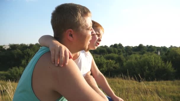 Der rothaarige Junge und sein Vater sitzen am grünen Rasen und zeigen auf etwas im Freien. Vater und Sohn ruhen sich auf der Wiese aus. Glückliche Familie, die zusammen Zeit in der Natur verbringt. Zeitlupe — Stockvideo