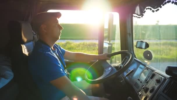 Perfil do condutor de camiões que atravessa a zona rural à hora do pôr do sol. Homem de chapéu controlando seu caminhão e aproveitando a viagem. Bela paisagem com luz solar brilhante no fundo. Lento movimento Fechar — Vídeo de Stock