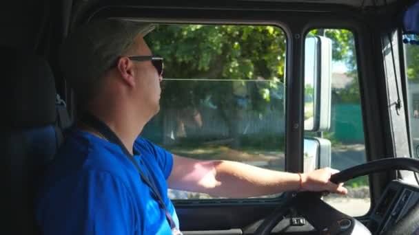 A következő profilja: kamionos vezetőfülke országúti lovaglás és élvezi az utazást napsütéses napon. Egy férfi sapkában és napszemüvegben figyeli a kamionját az utat figyelve. Lassú mozgás Oldalnézet — Stock videók