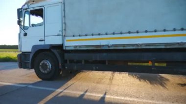 Kargo karavanıyla otoyolda gidip malları taşıyan kamyoneti kapatın. Akşam vakti kırsal yolda hızla ilerleyen beyaz bir kamyon. Kargo taşıma konsepti. Yavaş çekim kenar görünümü