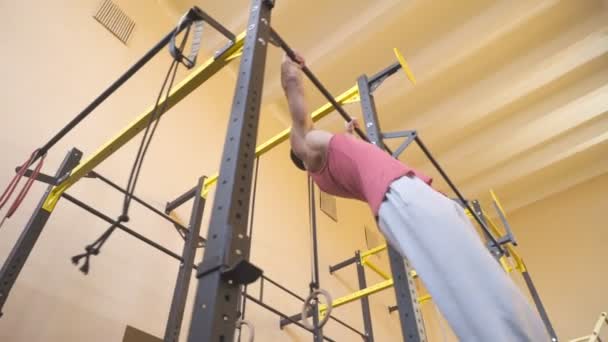 Hombre deportivo fuerte haciendo handstand en barra horizontal en el gimnasio. Gimnasta muscular en ropa deportiva haciendo acrobacias en interiores. Joven atleta mostrando rendimiento. Concepto de estilo de vida saludable y activo. Vista baja — Vídeos de Stock