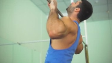 Spor giyimli kaslı bir sporcu spor salonunda barfiks çekiyor. Genç sporcu yatay çubukta egzersiz yapıyor. Güçlü sporcu içeride antrenman yapıyor. Sağlıklı ve aktif yaşam tarzı kavramı. Yavaşça kapat.