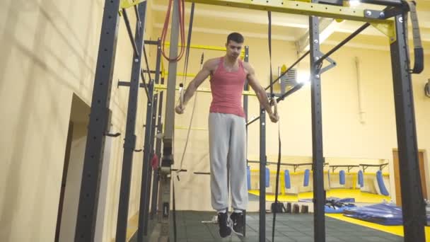 Atleta fuerte haciendo cruz en anillos gimnásticos en el gimnasio. Deportista musculoso en ropa deportiva mostrando acrobacias duras en interiores. Gimnasta masculino joven haciendo ejercicios acrobáticos. Concepto de estilo de vida saludable y activo — Vídeos de Stock