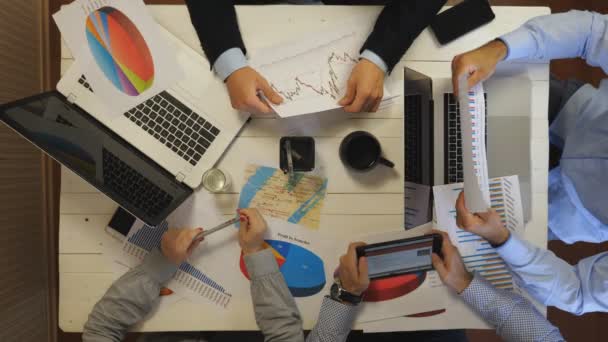 Male and female hands of entrepreneurs analyzing financial graphs at office. Group of young coworkers create corporate project sitting at table. Colleagues working on business development. Top view — Vídeo de Stock