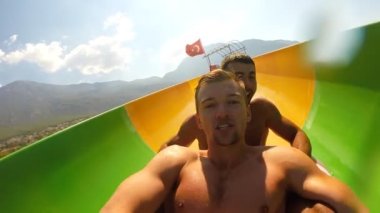 Arkadaşlarıyla birlikte Aquapark 'ta su kaydırağında kayan bir adam. Çocuklar eğleniyor ve dinlenme tesisinde dinleniyor. Arkadaşları yaz tatilinde kendini filme çekiyor. Yavaş çekim. Yakın çekim.