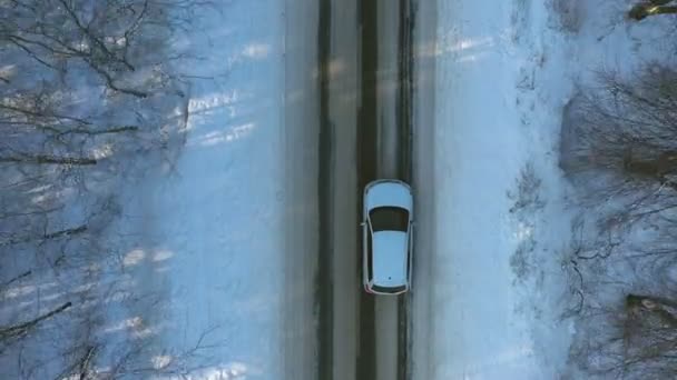 Primer plano del coche blanco que monta a través de la carretera del bosque nevado. SUV conducción en la hermosa ruta del campo en el día invernal. Viajes de invierno en la naturaleza. Concepto de viaje en familia. Vista superior plano aéreo — Vídeos de Stock