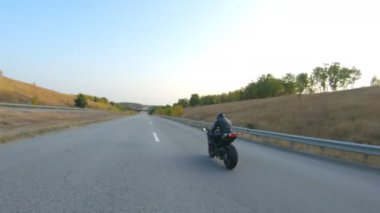 Anayolda motosiklet süren motosikletliyi takip edin. Motosikletli, kır yolunda motosikletiyle yarışıyor. Yolculuk sırasında bisiklet süren adam. Yolculukta özgürlük ve macera kavramı. Hava görüntüsü