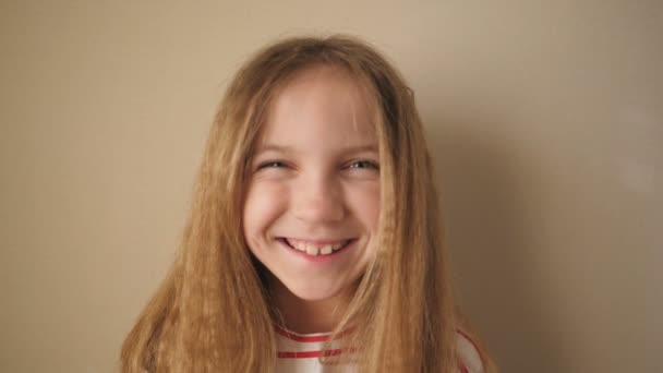 Joyful blonde meisje kijken in de camera en lachen indoor. Portret van een klein vrouwelijk kind tegen de achtergrond van de muur. close-up emoties van glimlachend kind met blije uitdrukking op haar gezicht — Stockvideo