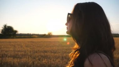 Gün batımında buğday tarlasında yürüyen güzel bir kadın. Yaz akşamının tadını çıkaran kaygısız bir kızın profili ve doğal ortamda özgürlüğün. Meadow 'da gezinen bir kadın. Yan Görünüm Kapat