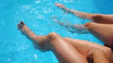 Havuzun kenarında oturan ve ayaklarını suya sokan genç kadınlar. İnce bronzlaşmış bacakları olan iki kız lavabonun yanında dinleniyor. Hanımlar tatilin tadını çıkarıyor. Yaz tatili kavramı. Yavaş çekim