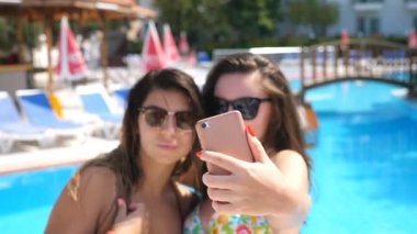 Çekici esmerler akıllı telefonda selfie portresi çekiyorlar. Yaz tatilinde fotoğraf çeken kaygısız genç kadınlar. Kameraya poz veren güneş gözlüklü güzel bayanlar. İki kız arkadaş birlikte dinleniyor.
