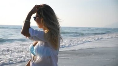 Güneş gözlüklü çekici bayan deniz manzaralı arka planda gülümsüyor ve okyanus kıyısında geziniyor. Keyfi yerinde bir kadının portresi özgürlüğün tadını çıkarıyor ve sahilde eğleniyor. Tatil köyünde eğlenen tatlı kız.