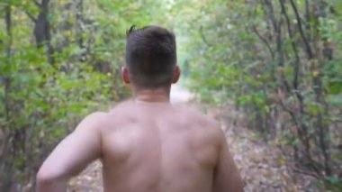 Sonbahar ın başlarındaki ormanda patikada koşan genç kaslı bir adam. Tanınmayan sporcu doğada yol boyunca koşuyor. Atletik adam açık havada egzersiz. Sağlıklı aktif yaşam tarzı kavramı. Arka görüş