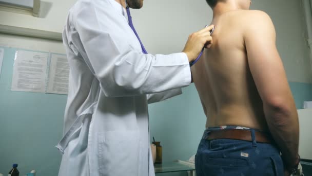 Le médecin vérifie le type dans son bureau à l'hôpital. Médecin examinant un jeune patient masculin avec stéthoscope. Travailleur médical à l'écoute des battements de coeur de l'homme. Gros plan — Video