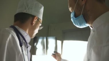 Kafkasyalı iki doktor MRI resmine bakıp bunu tartışıyor. Erkek doktorlar röntgen görüntülerine bakarken birbirlerine danışıyorlar. Hastanedeki tıp çalışanları röntgen izlerini inceliyor. Arka plan görünümü